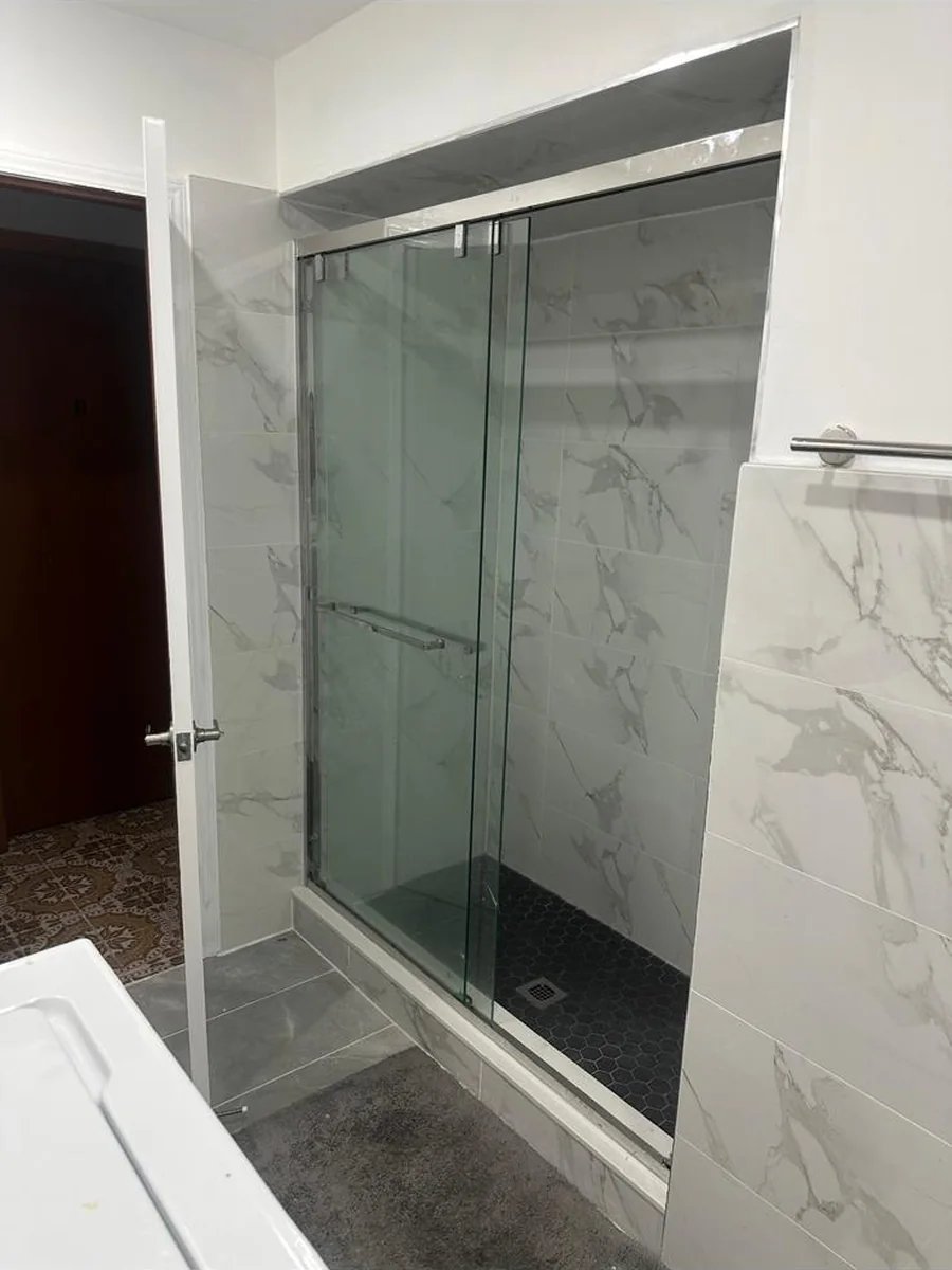 Glass shower enclosure with marble-look wall tile and a dark mosaic floor