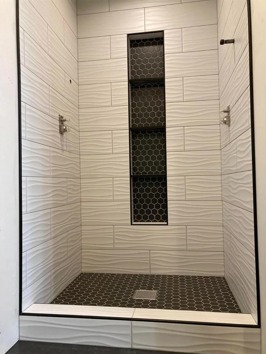 White tiled shower with a black mosaic floor and recessed vertical niche